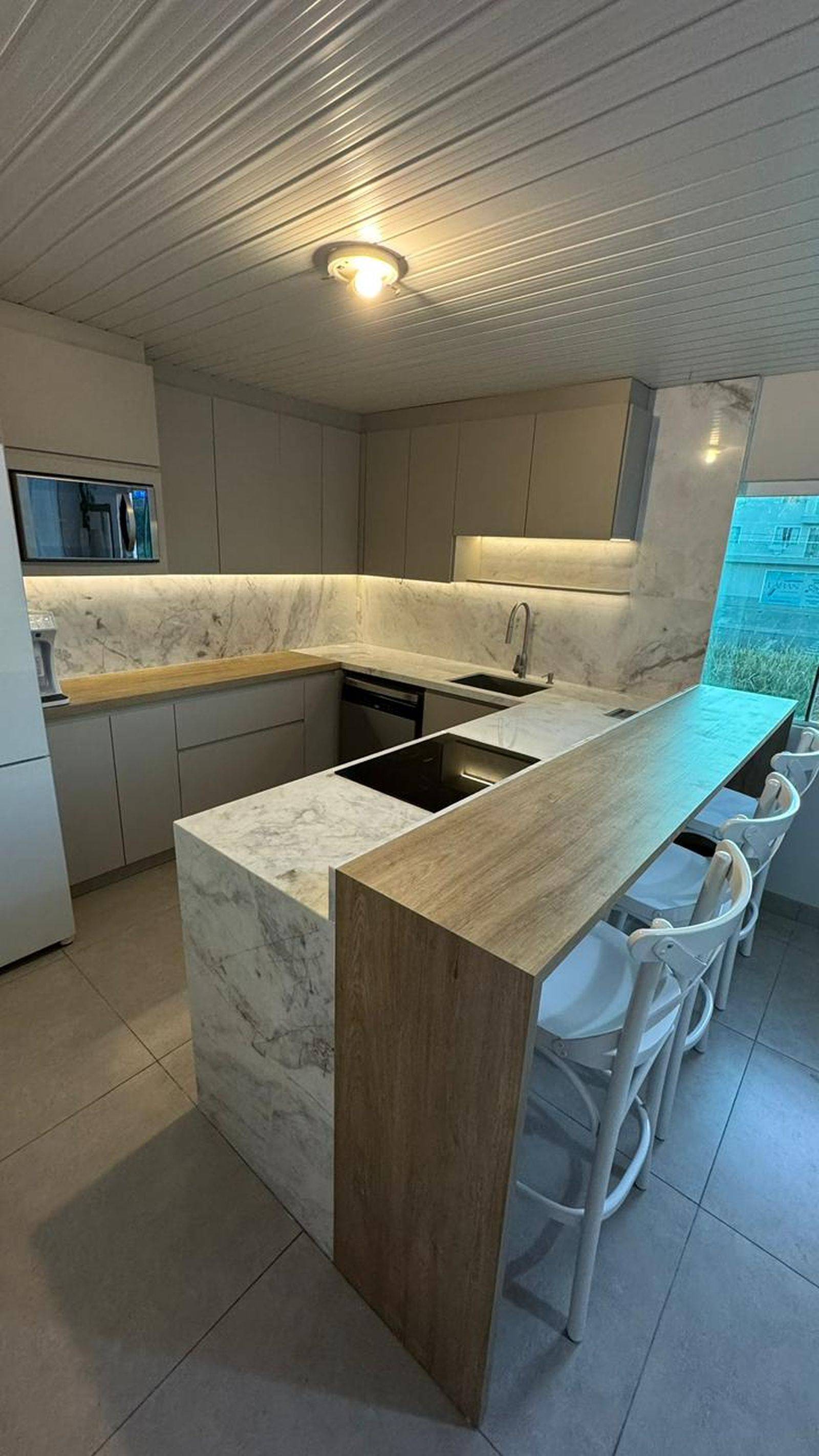 Cozinha planejada em mármore branco Paraná com ilha central iluminada e veios contínuos.